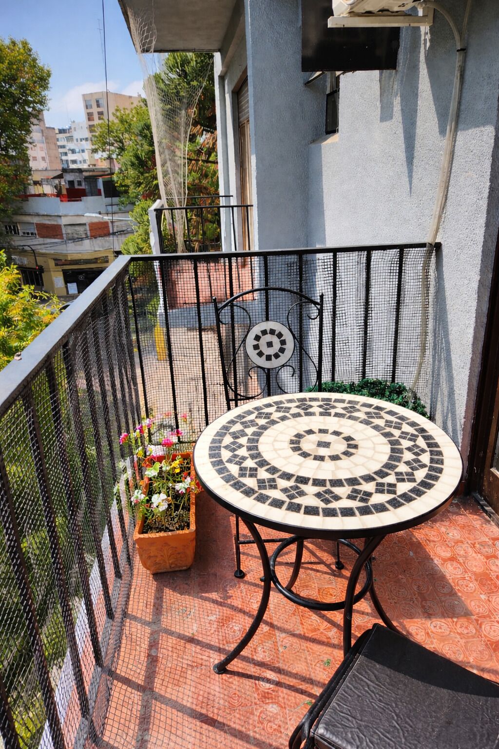 A balcony with a round table and chairs, a potted plant, and a metal fence.