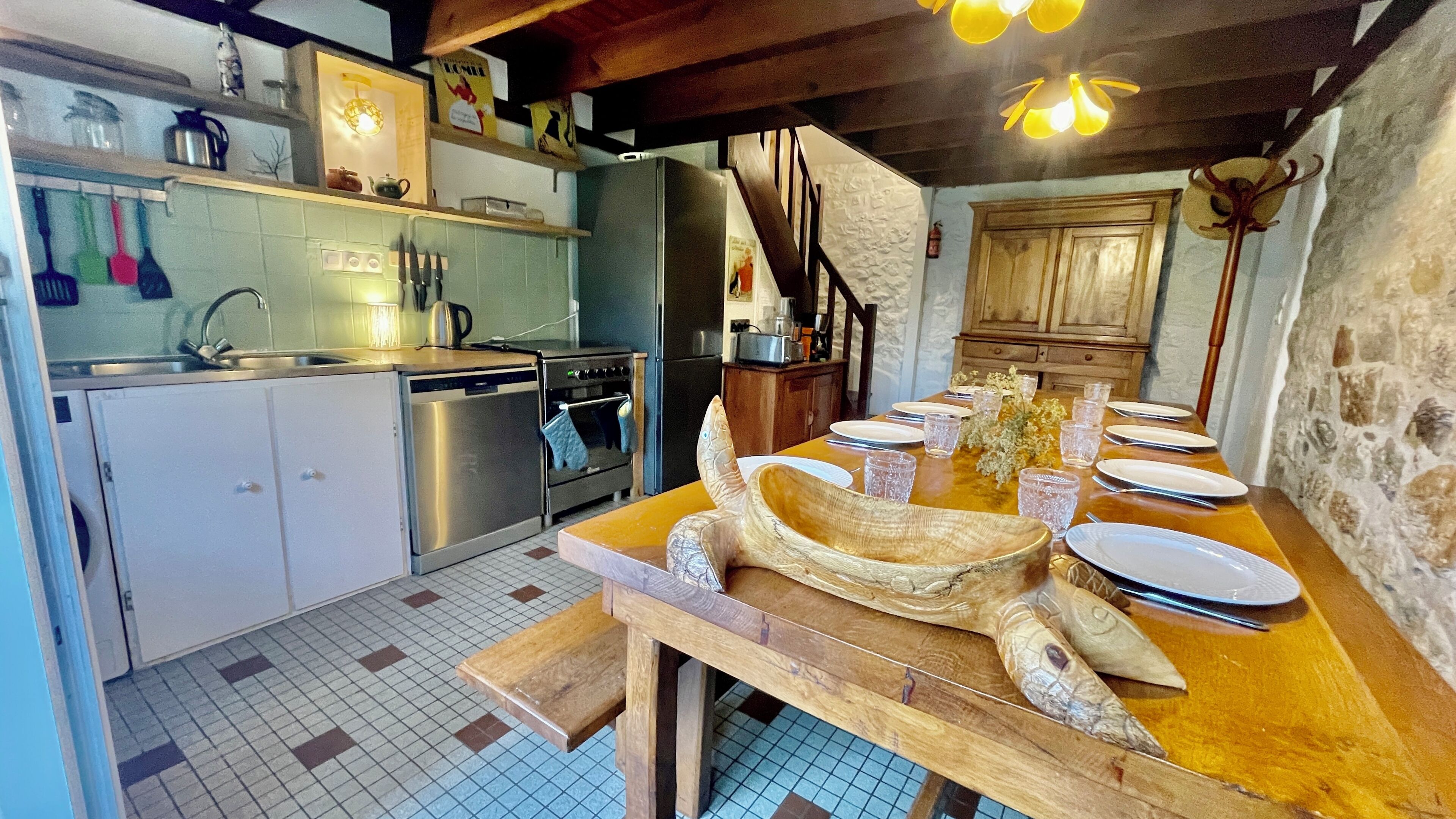 Uma cozinha com uma mesa de jantar posta para quatro pessoas, geladeira, fogão e pia.