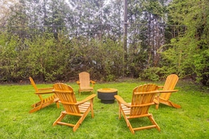 A backyard with four wooden Adirondack chairs arranged around a circular fire pit.