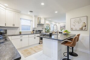 A modern kitchen with white cabinets, a granite countertop, a stainless steel range, and a large island with bar stools.