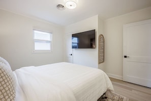 A bedroom with a bed, a window, a door, and a mounted TV.