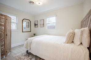 A bedroom with a bed, a wooden wardrobe, a mirror, and framed pictures on the wall.