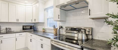 Una cocina moderna con armarios blancos, estufa de acero inoxidable y horno empotrado.