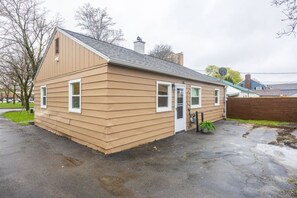 A single-story building with a gabled roof, a front door, and a small front yard with a potted plant.
