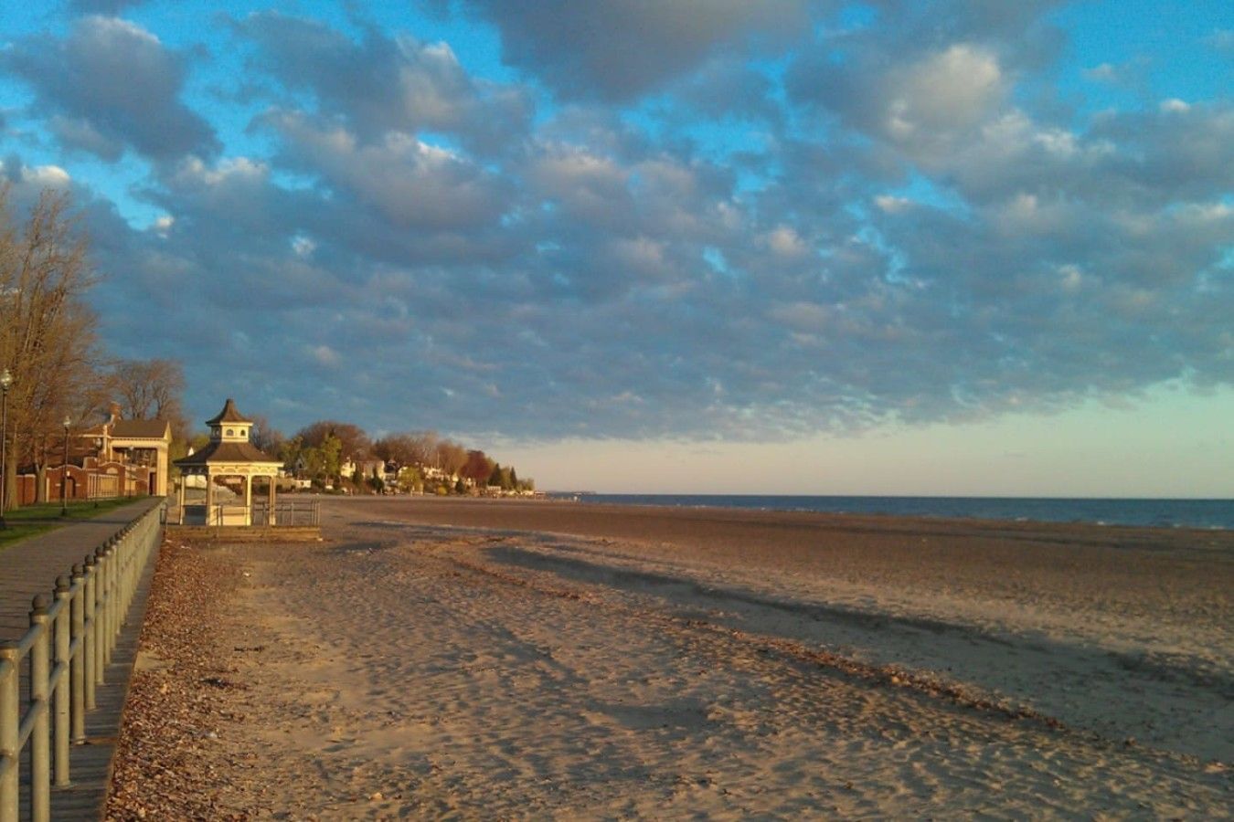 Une promenade en bord de mer agrémentée d’un kiosque, d’une clôture et de bâtiments visibles au loin.