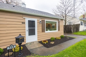 A single-story house with a beige siding exterior, a white front door, and a small front yard with a pathway leading to the door.