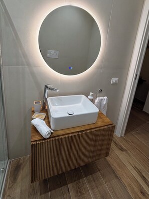 Ein modernes Badezimmer mit einem Holzkosmetikschrank, einem weißen Waschbecken und einem runden Spiegel mit integrierter Beleuchtung.