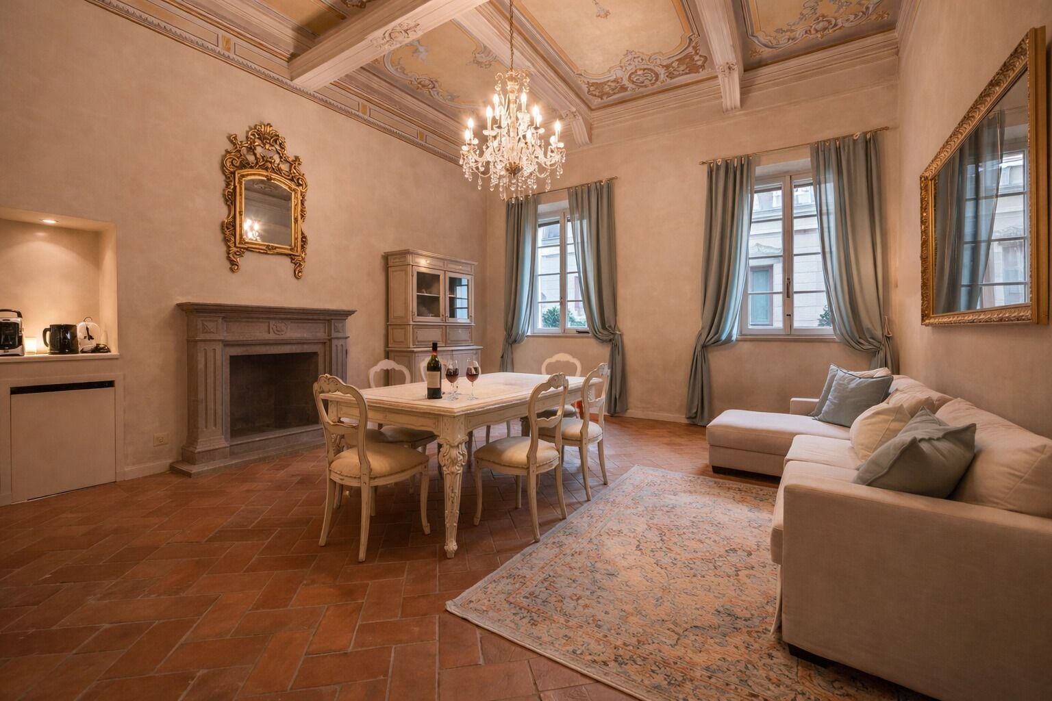 Une pièce spacieuse comprenant une table à manger, des chaises, une cheminée, un canapé et un lustre.