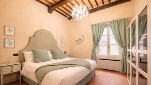 A bedroom with a bed, nightstands, a chandelier, a window with curtains, and a wall-mounted clock. - Avignonesi - Chic Frescoed Palace - 2BR 2BA - Heart of Montepulciano (Montepulciano)