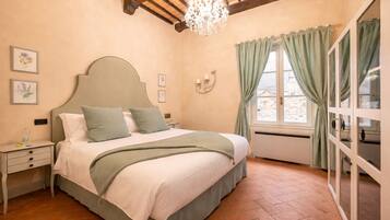 Une chambre à coucher comprenant un lit, des tables de chevet, un lustre, une fenêtre avec des rideaux et une horloge murale.