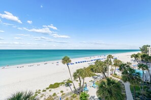 A beach view with a white sandy shore, clear blue water, and a row of blue umbrellas. - Sand Castle Oceanfront Retreat (Indian Shores)