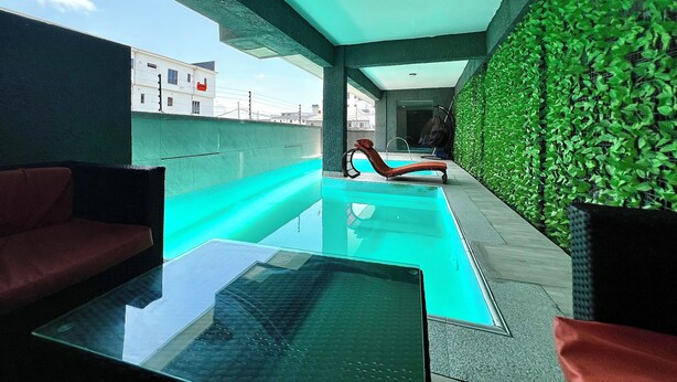 Uma área de piscina no terraço, com mesa de vidro, espreguiçadeiras e parede verde.