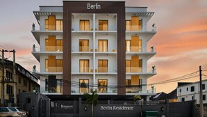 Um edifício moderno de vários andares com o nome 'Berlin Residence' na fachada, apresentando um design simétrico com varandas e grandes janelas.
