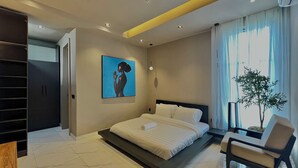 Um quarto moderno com cama, uma cadeira, uma planta e um quadro na parede.