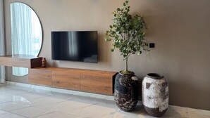 Uma sala de estar moderna com uma televisão de tela plana na parede, console de madeira embaixo e dois vasos grandes no chão.