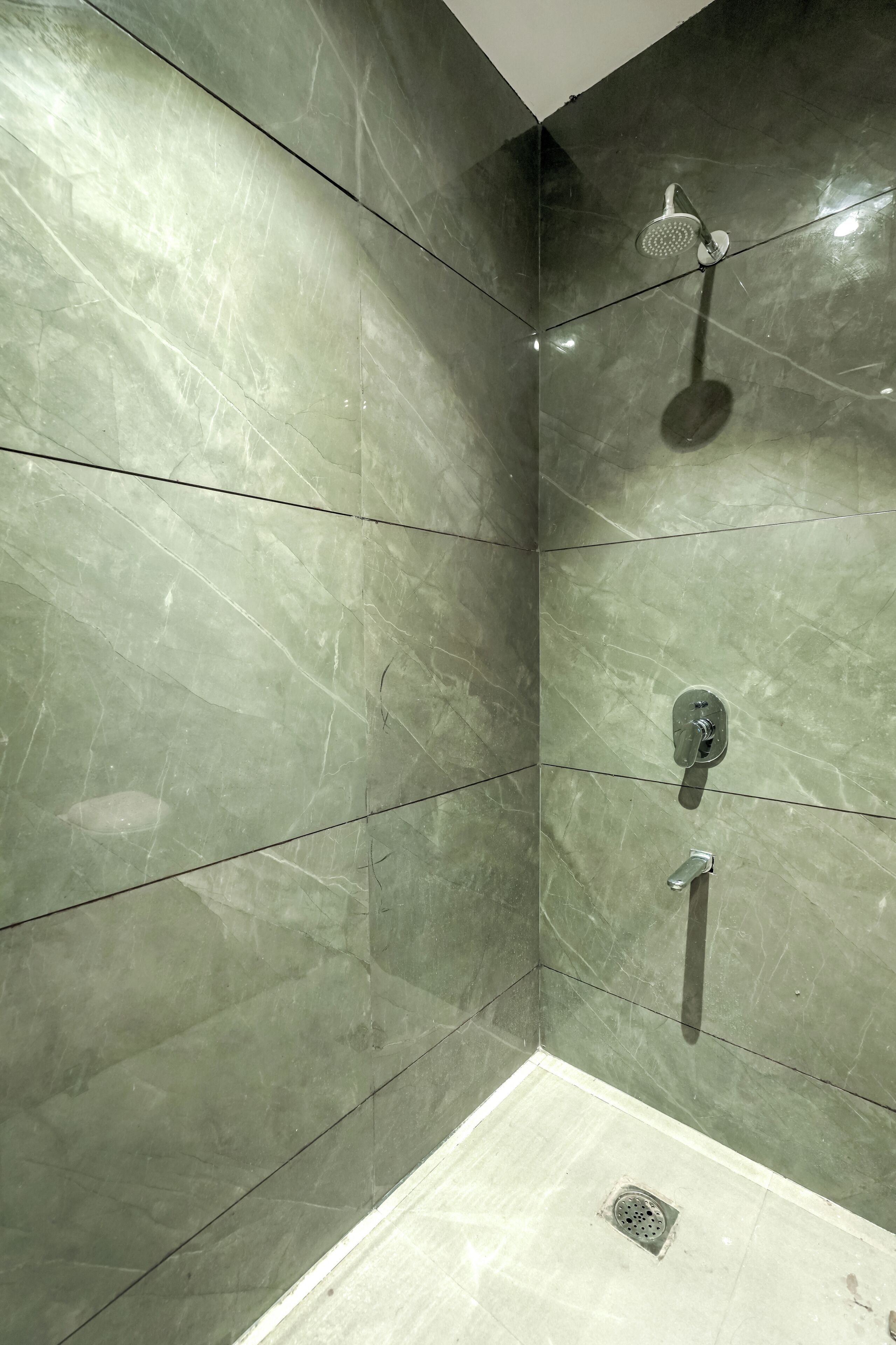 Un baño con azulejos de mármol verde, un cabezal de ducha y desagüe.