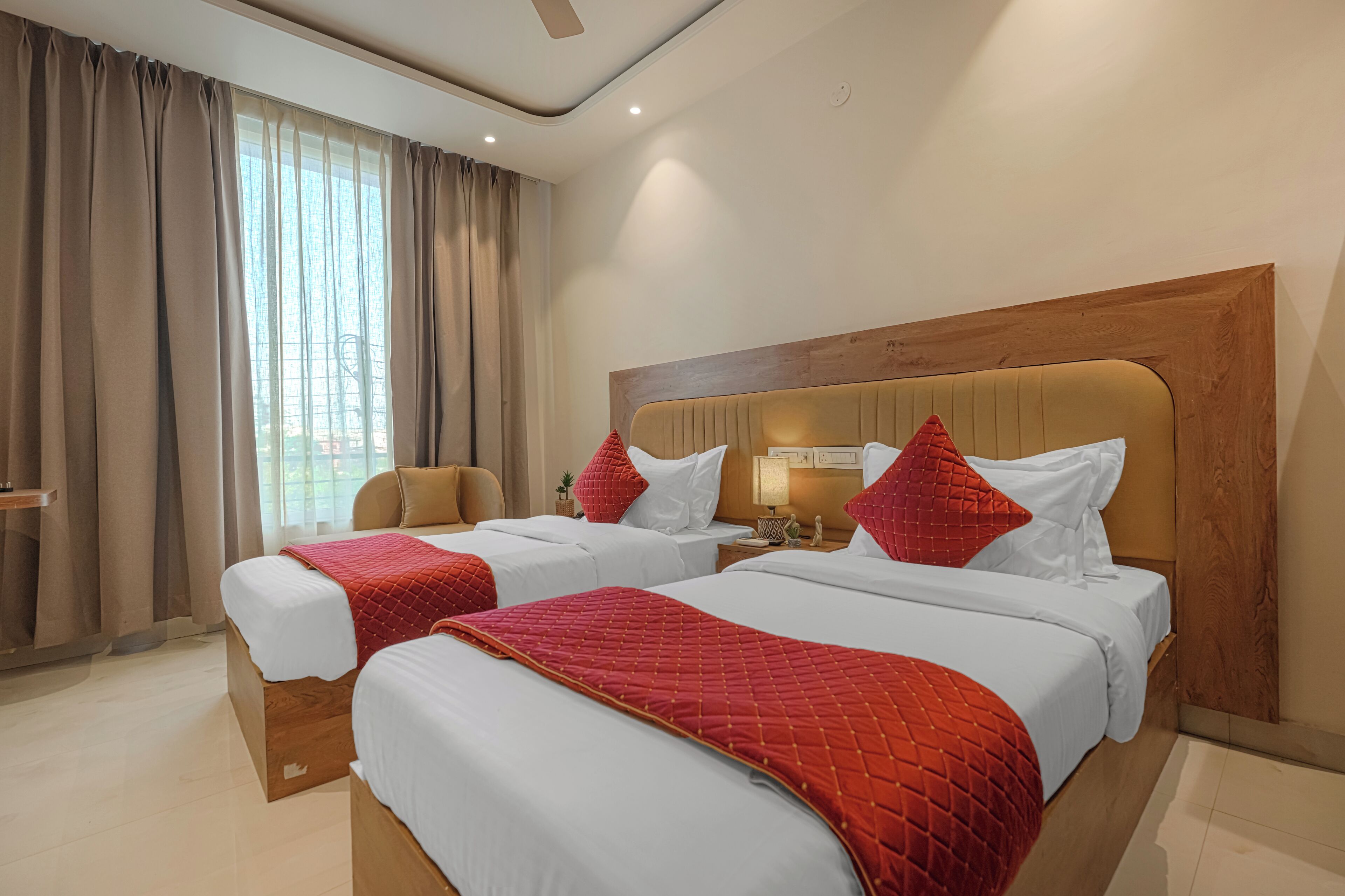 A hotel room with two beds, a wooden headboard, a nightstand, a chair, and a large window with curtains.