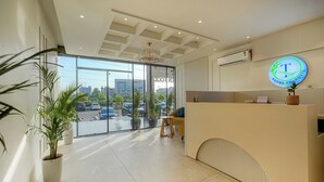 A hotel reception area with a modern design, a reception desk, a chandelier, potted plants, and a view of the parking lot. - Hotel Tranquil Airport Road Sector 66 Mohali Chandigarh (Mohali)
