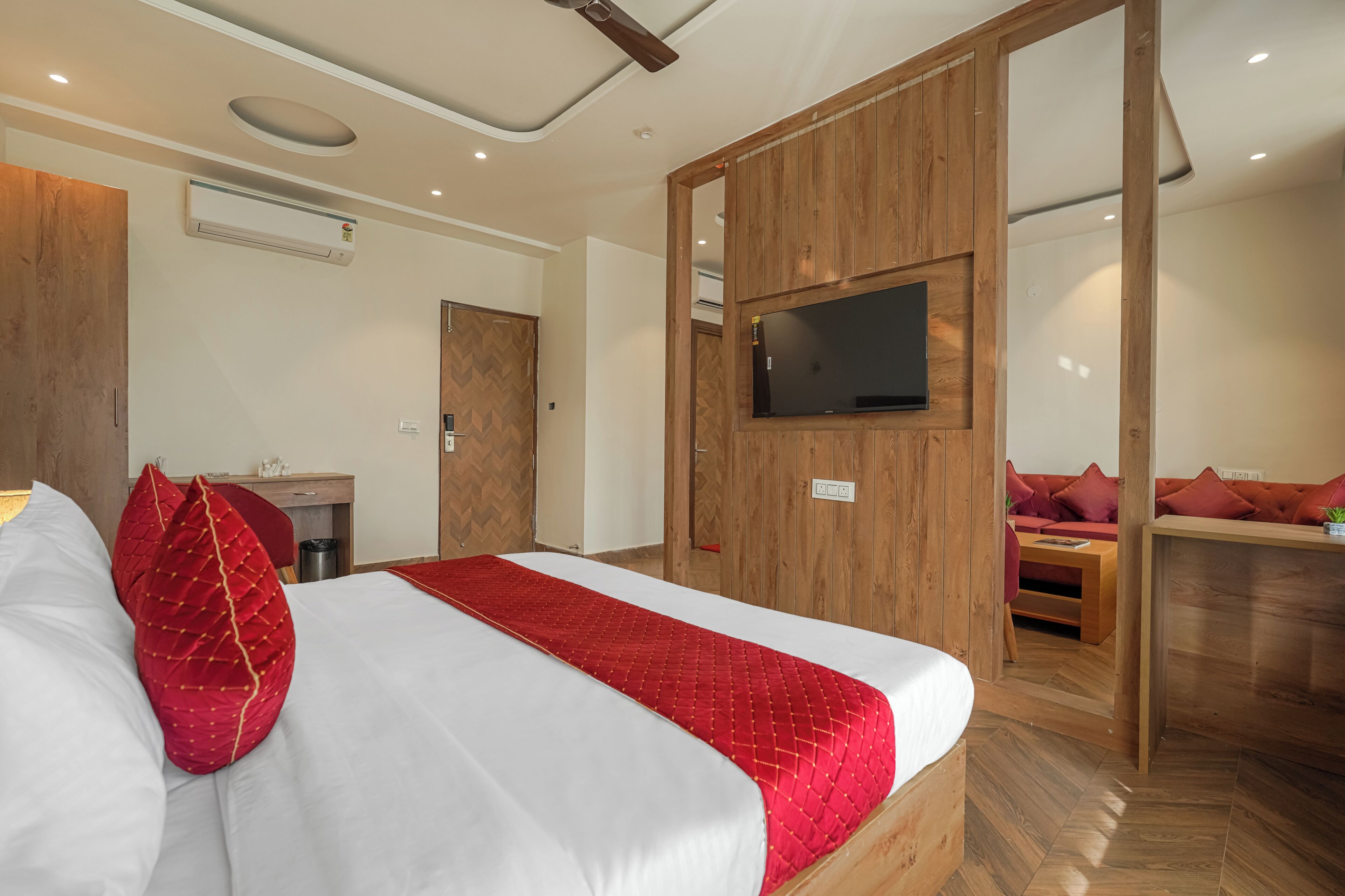 Una habitación de hotel con una cama, un televisor montado en la pared, un armario de madera y una zona de estar con sofá.