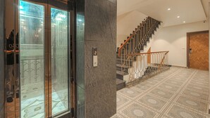 A modern interior with a marble staircase, a glass elevator, and a patterned floor. - Hotel Tranquil Airport Road Sector 66 Mohali Chandigarh (Mohali)