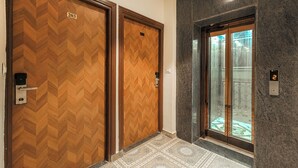 Two wooden doors with a chevron pattern, a marble wall, and an elevator with a glass door. - Hotel Tranquil Airport Road Sector 66 Mohali Chandigarh (Mohali)