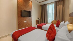 A hotel room with two beds, a TV mounted on a wooden wall, a window with curtains, and a ceiling fan. - Hotel Tranquil Airport Road Sector 66 Mohali Chandigarh (Mohali)