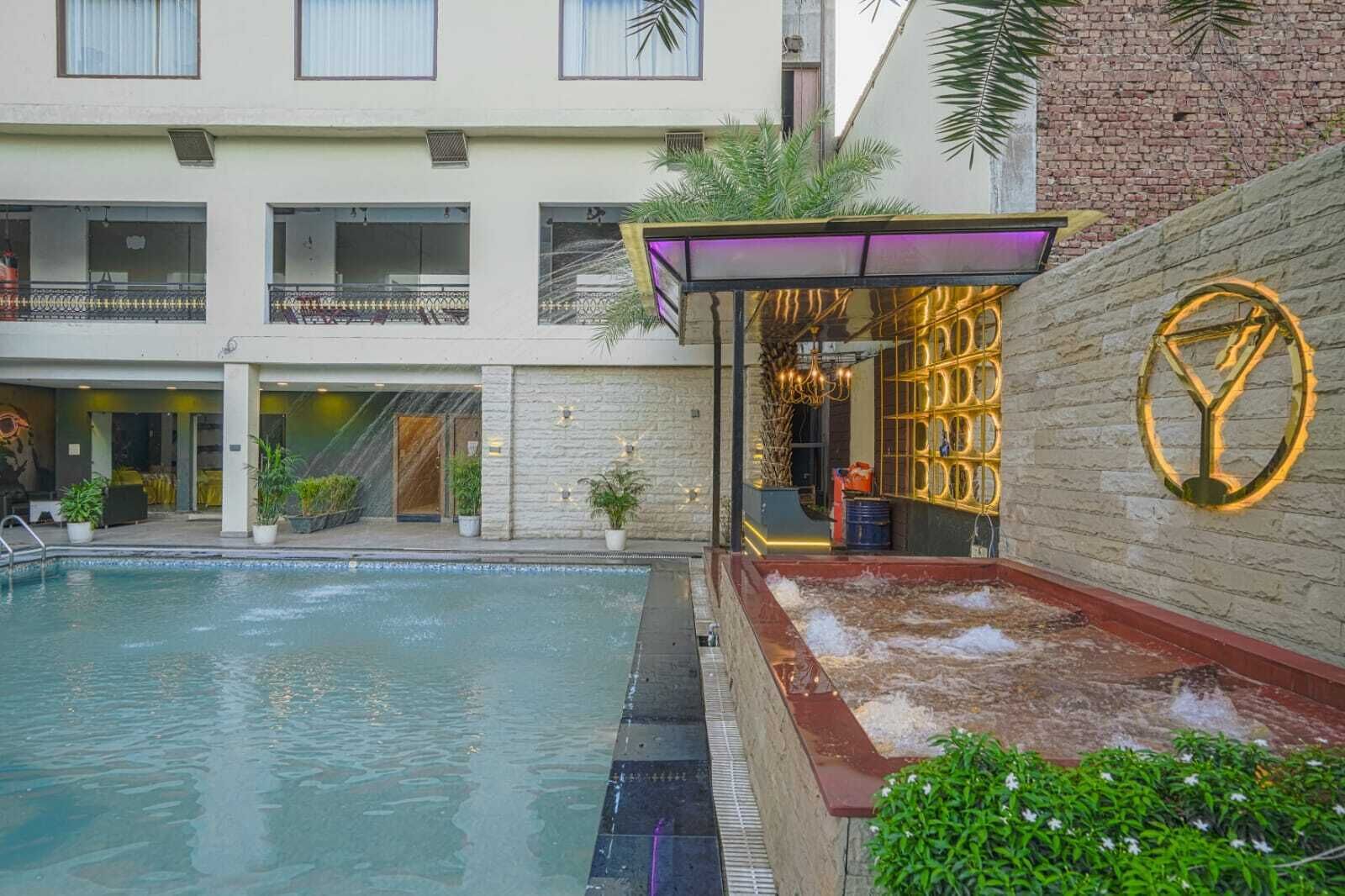 Una piscina con una zona hundida, un área de estar cubierta con un muro decorativo y un muro de ladrillo con un emblema circular.