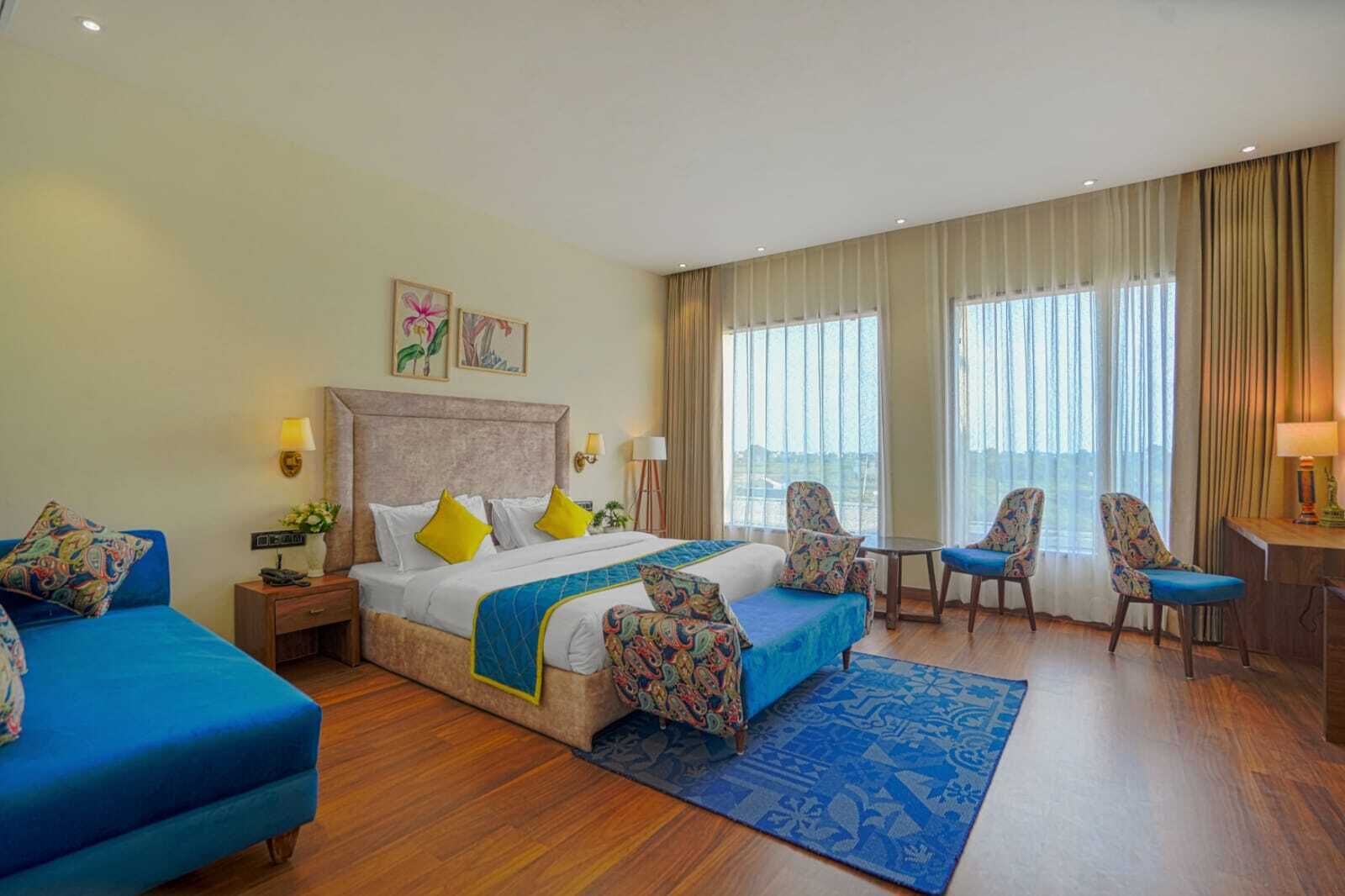 A hotel room with a bed, two blue sofas, a desk, and a view of the city.