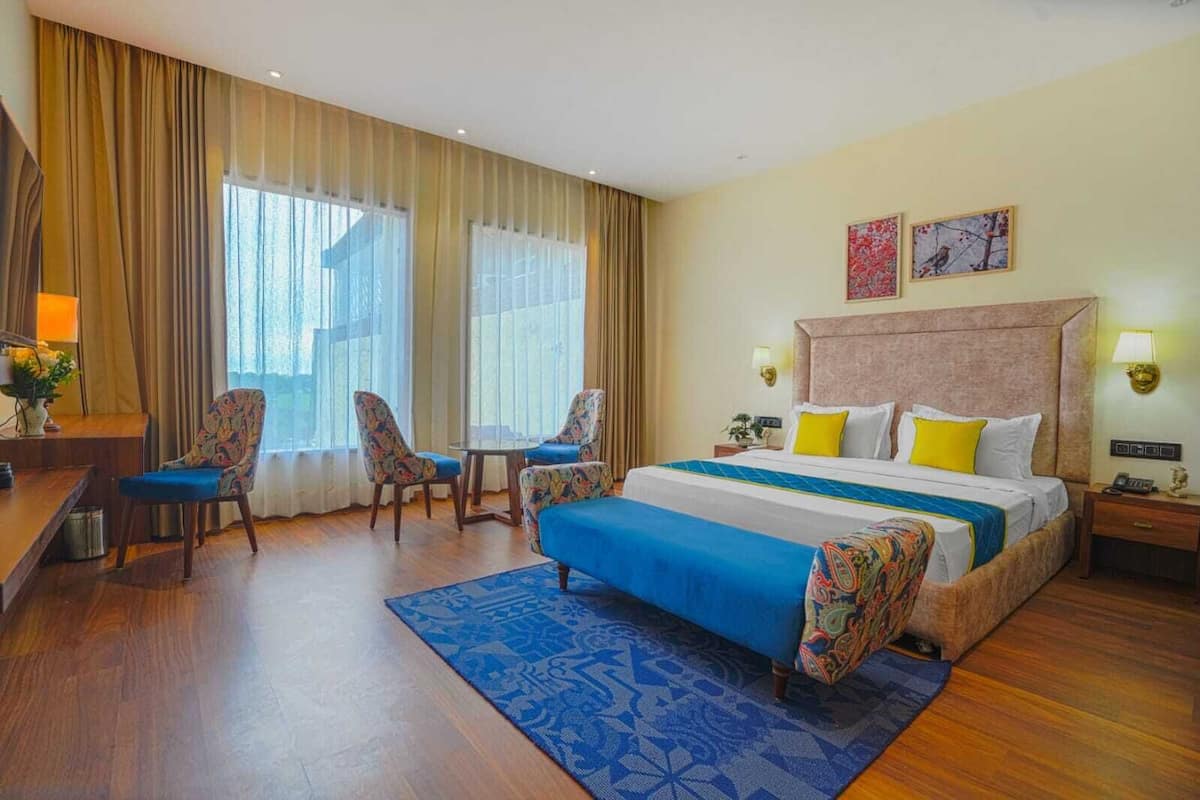 Habitación de hotel con una cama grande, dos sillones, un escritorio y una ventana con cortinas.