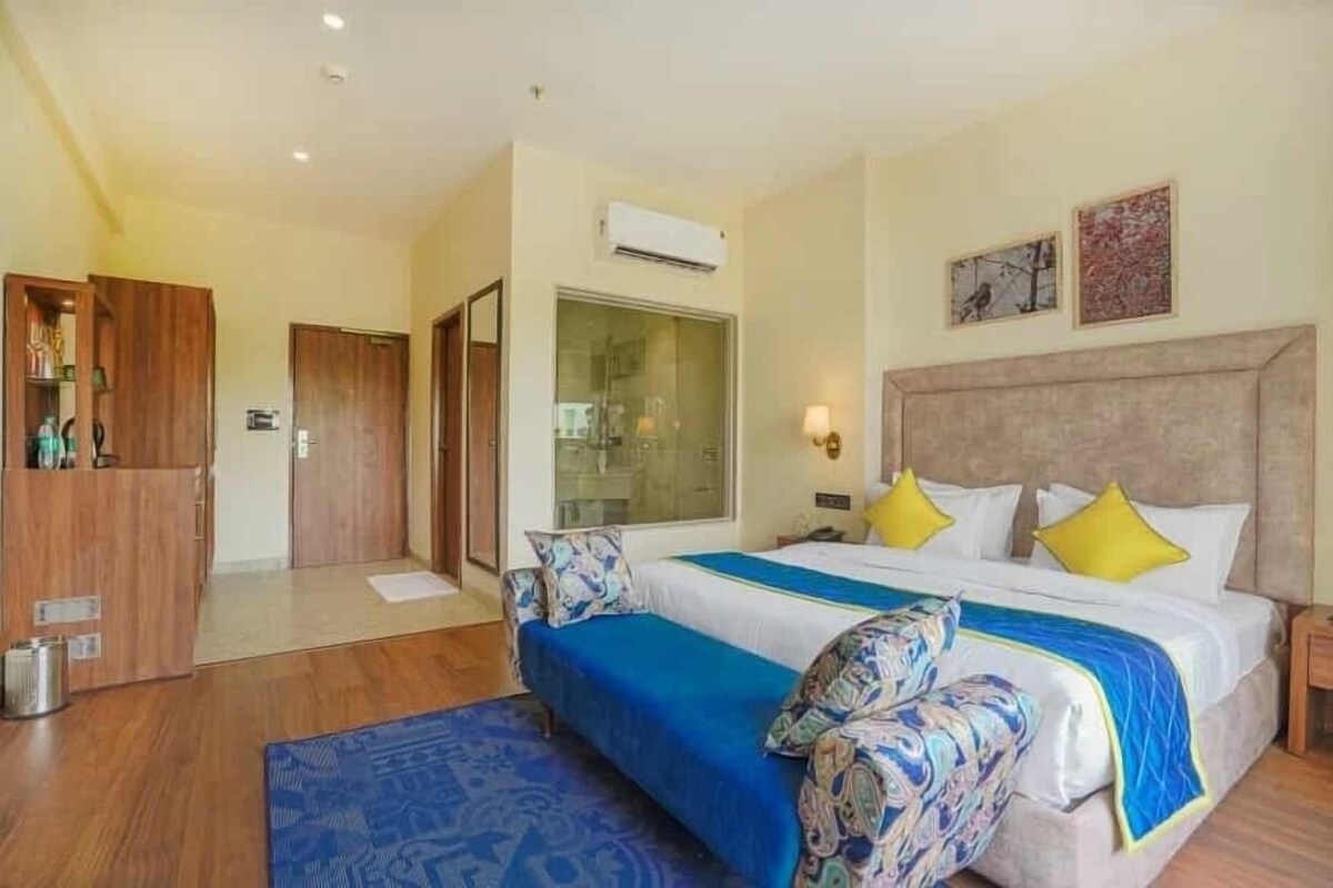 A hotel room with a large bed, a wooden wardrobe, a glass door, and a wall-mounted air conditioner.