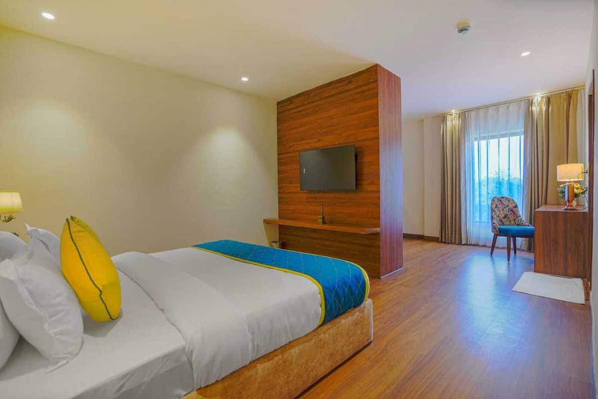 Habitación de hotel con cama, televisión montada en un panel de madera, escritorio con lámpara y una silla.
