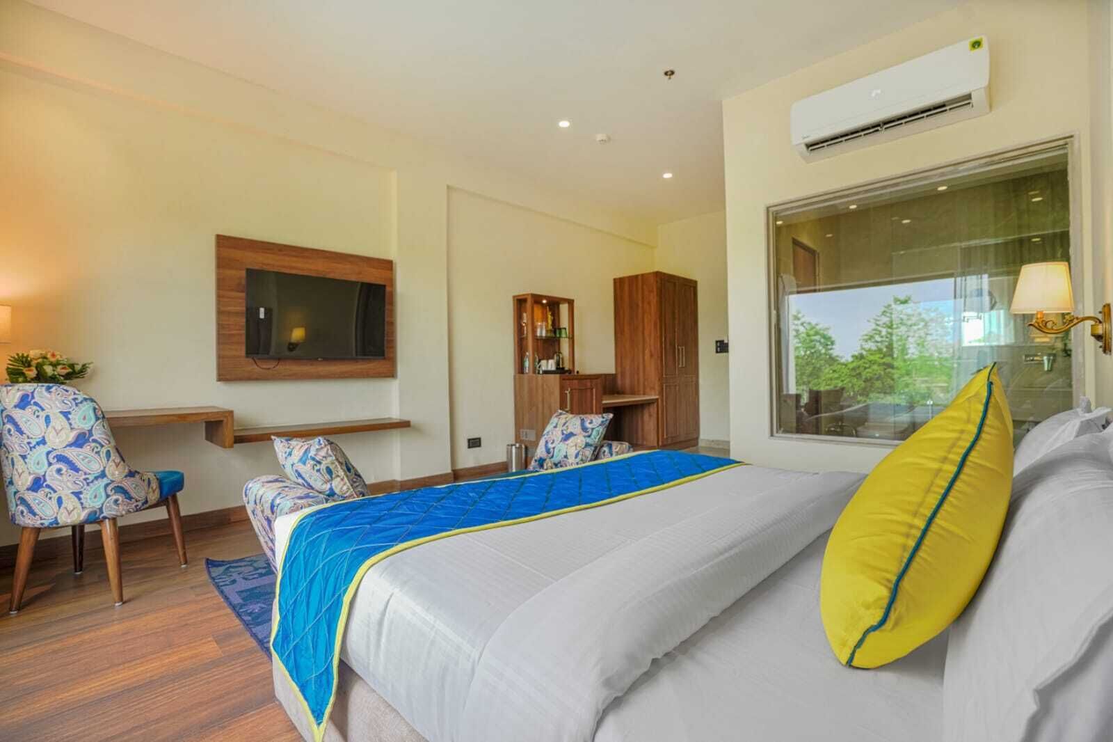 A modern hotel room with a large bed, a desk, a wardrobe, and a window with a view.