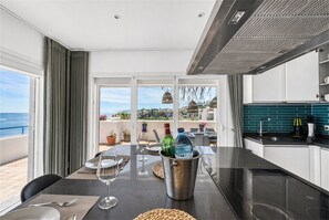 A modern kitchen with a dining area, large windows, and a view of the sea. - 3180 Duplex Penthouse with Panoramic Sea Views (Casares)