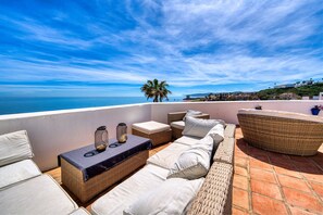 A rooftop terrace with wicker furniture, a table with candles, and a view of the sea. - 3180 Duplex Penthouse with Panoramic Sea Views (Casares)
