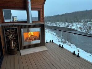 A wooden deck with a fireplace, a glass balustrade, and a view of a river and snowy landscape. - Luxury at Davis Riverwalk (Davis)