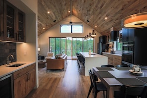 Une cuisine moderne avec un plafond en bois, un coin repas et une grande fenêtre donnant sur un espace verdoyant.