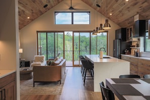 A spacious kitchen with a large island, wooden ceiling, and large windows offering a view of the outdoors. - Luxury at Davis Riverwalk (Davis)