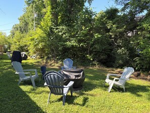 A grassy outdoor area with Adirondack chairs and a covered grill.