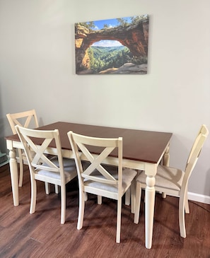 A dining table with four chairs, a painting of a natural landscape, and a wooden floor. - The Lazy Hiker I Cozy 2BR I 15m to RRG I Wi-Fi (Stanton)