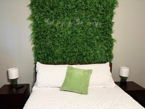 Uma cama com roupa de cama branca, um travesseiro verde e uma parede coberta por folhagem verde.