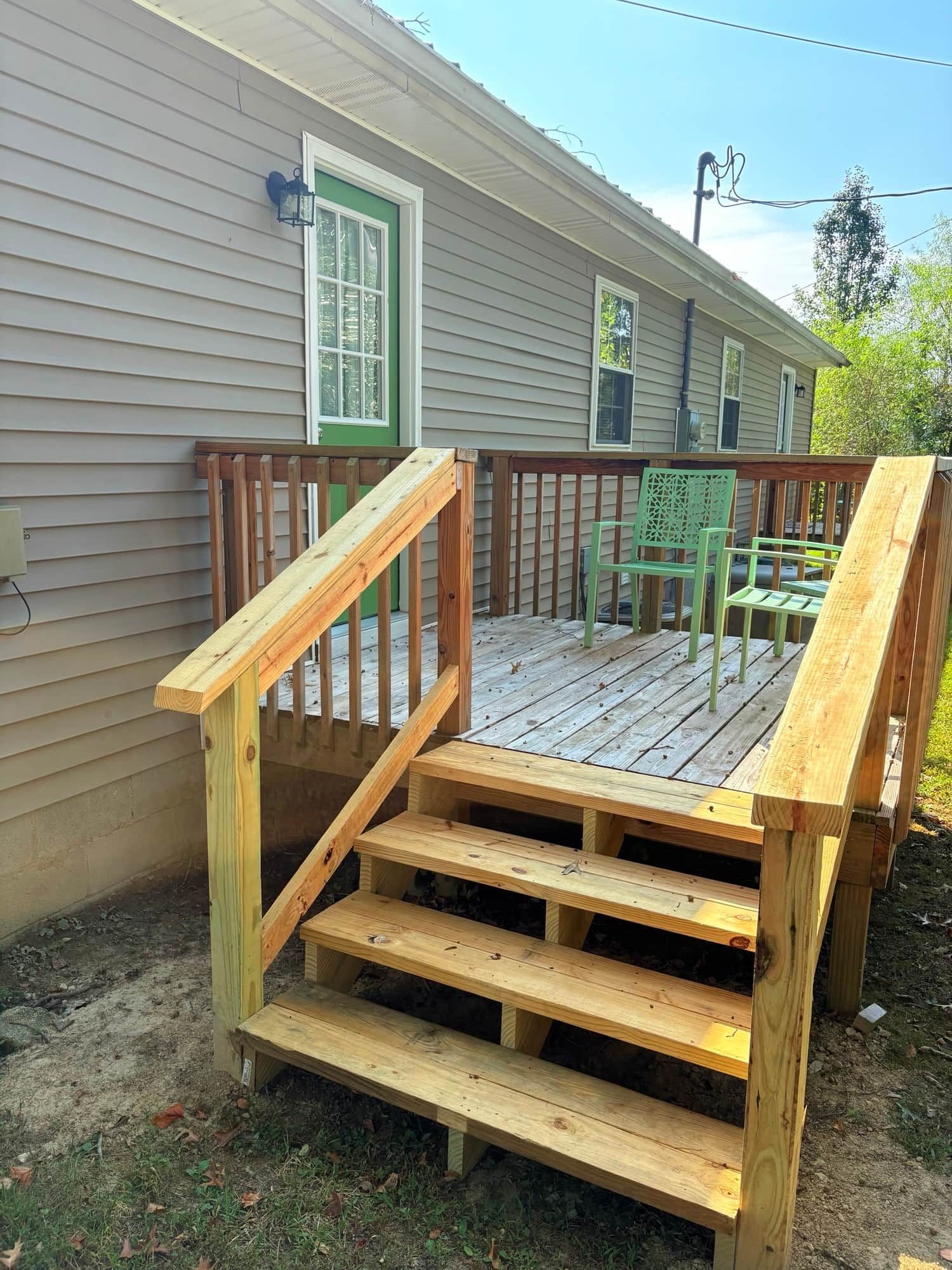Une terrasse en bois avec une rampe menant à une porte verte, le tout entouré d’une clôture.