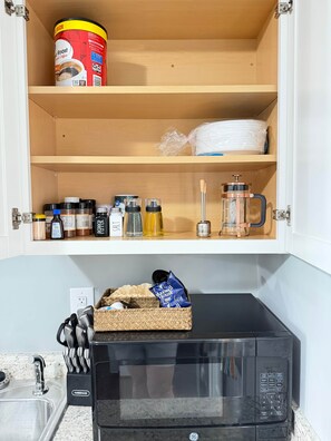 Uma cozinha com micro-ondas, cafeteira e um armário com diversos utensílios.