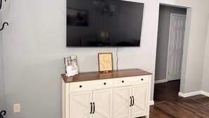 A room with a TV mounted on the wall, a wooden cabinet with drawers, and a door in the background. - The Lazy Hiker I Cozy 2BR I 15m to RRG I Wi-Fi (Stanton)