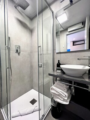 Ein modernes Badezimmer mit einer gläsernen Duschkabine, einem weißen Waschbecken und einem Spiegel darüber.