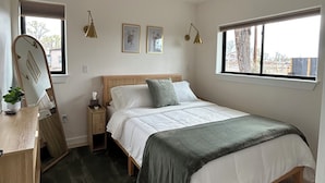 Un dormitorio con cama, mesitas de noche, escritorio, espejo y ventilador de techo.