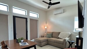 Una sala de estar moderna con comedor, ventilador de techo, sofá, televisor y chimenea.