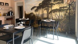 A dining area with a table set for two, a coffee machine, and a mural of trees on the wall. - Les libellules (Gémil)