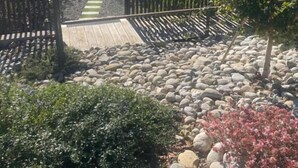 A garden pathway with a wooden fence, a stone wall, and various plants. - Les libellules (Gémil)