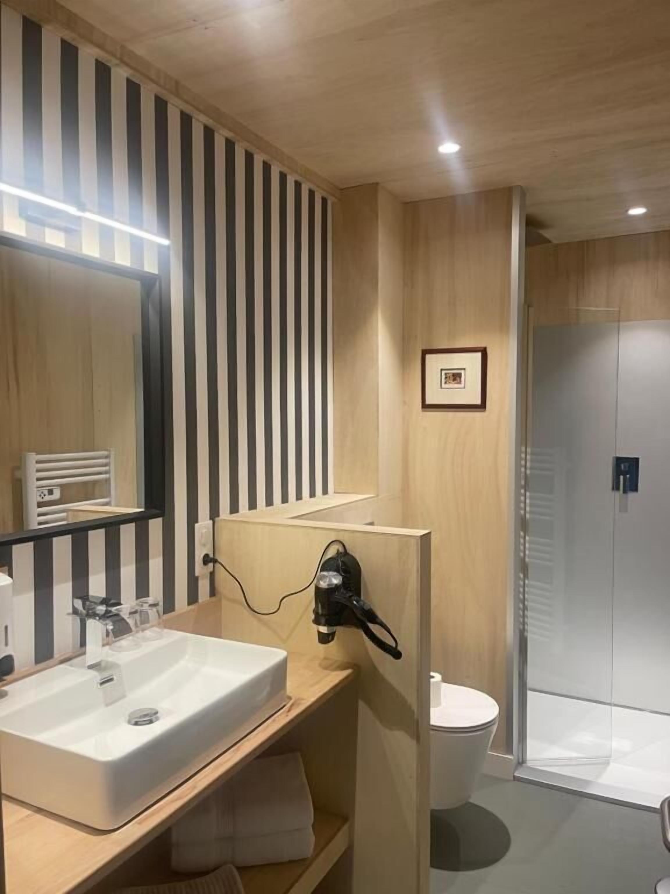 Un baño moderno con un espejo grande, un lavamanos, un perchero para toallas y una zona de ducha.