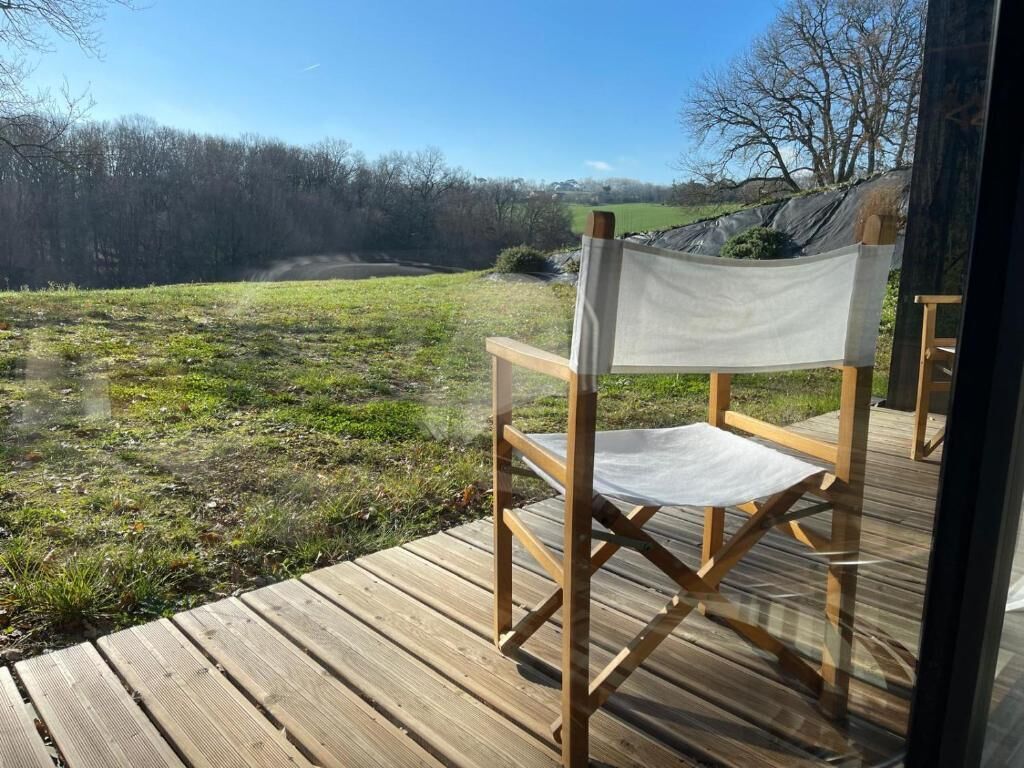 A wooden deck with a folding chair facing a grassy field and trees.